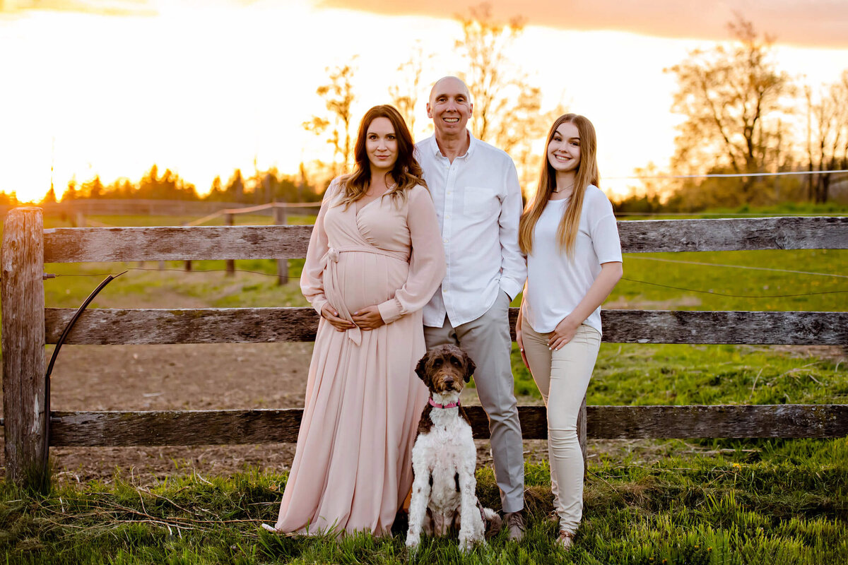 mom and dad with teenage daughter and dog on a farm for their outdoor maternity photography session in Burlington, On