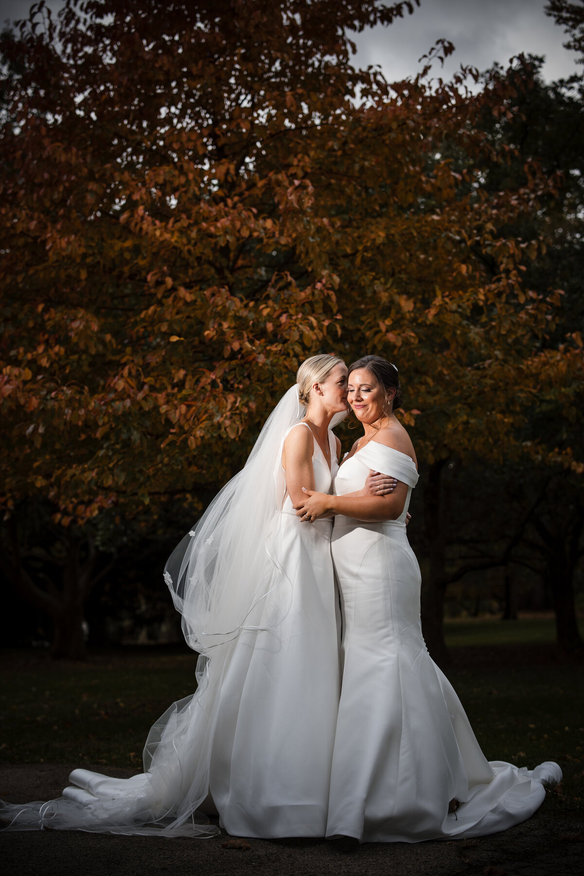 Two brides embrace outdoors at a  Fairmount Park Horticulture Center wedding