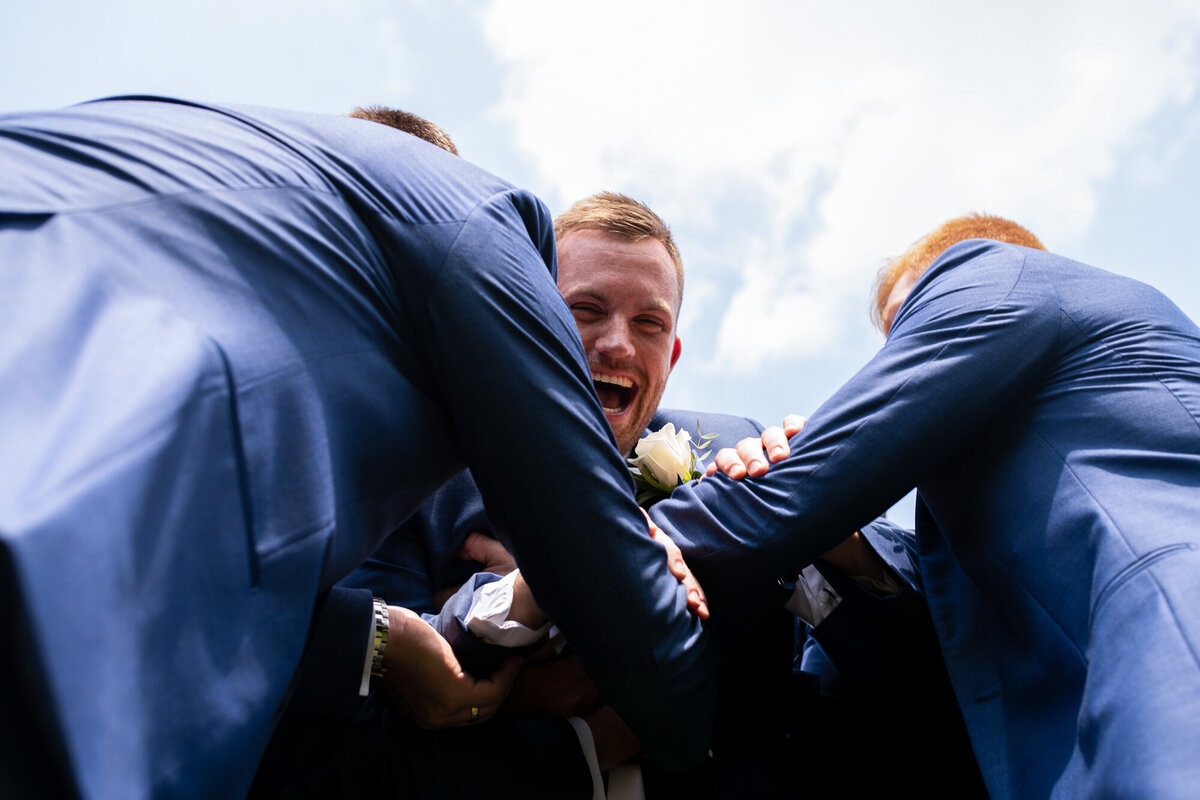 Groom laughs as his groomsmen catch him after tossing him in the air