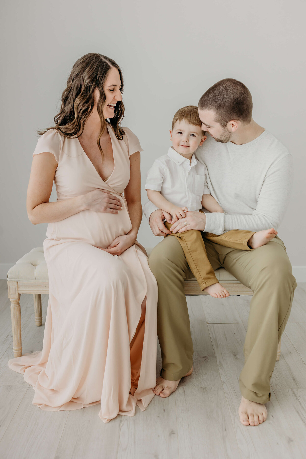 Family sitting on bench in photography studio for maternity pictures