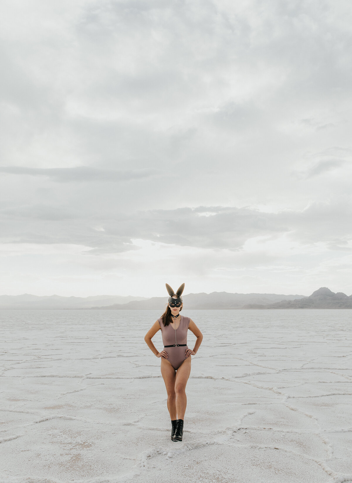 A woman walking towards the camera with her hands on her hips and a leather bunny mask on her face.