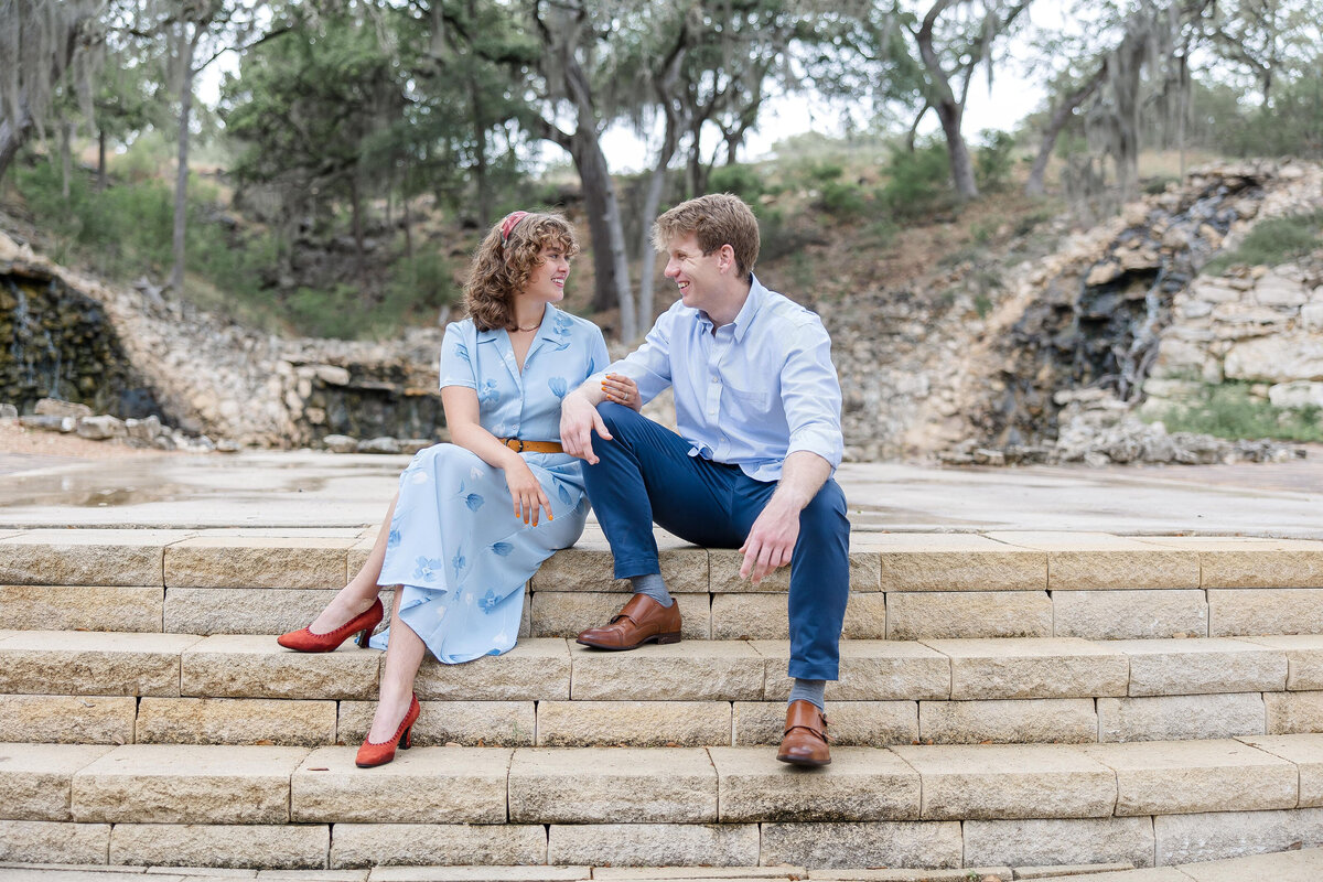 wedding engagement blue dress and red shoes engaged couple sit at Hayes Hollow Hidden Falls in Spring Branch Texas by firefly Photography