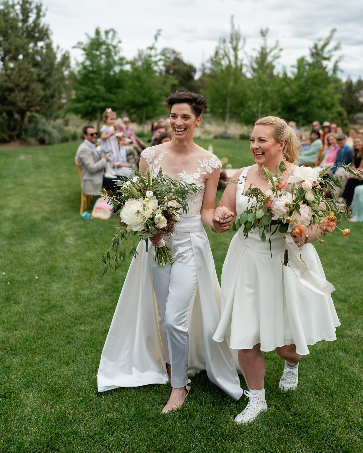 One bride in a pantsuit with train, and another in a short white dress for their Bend micro wedding