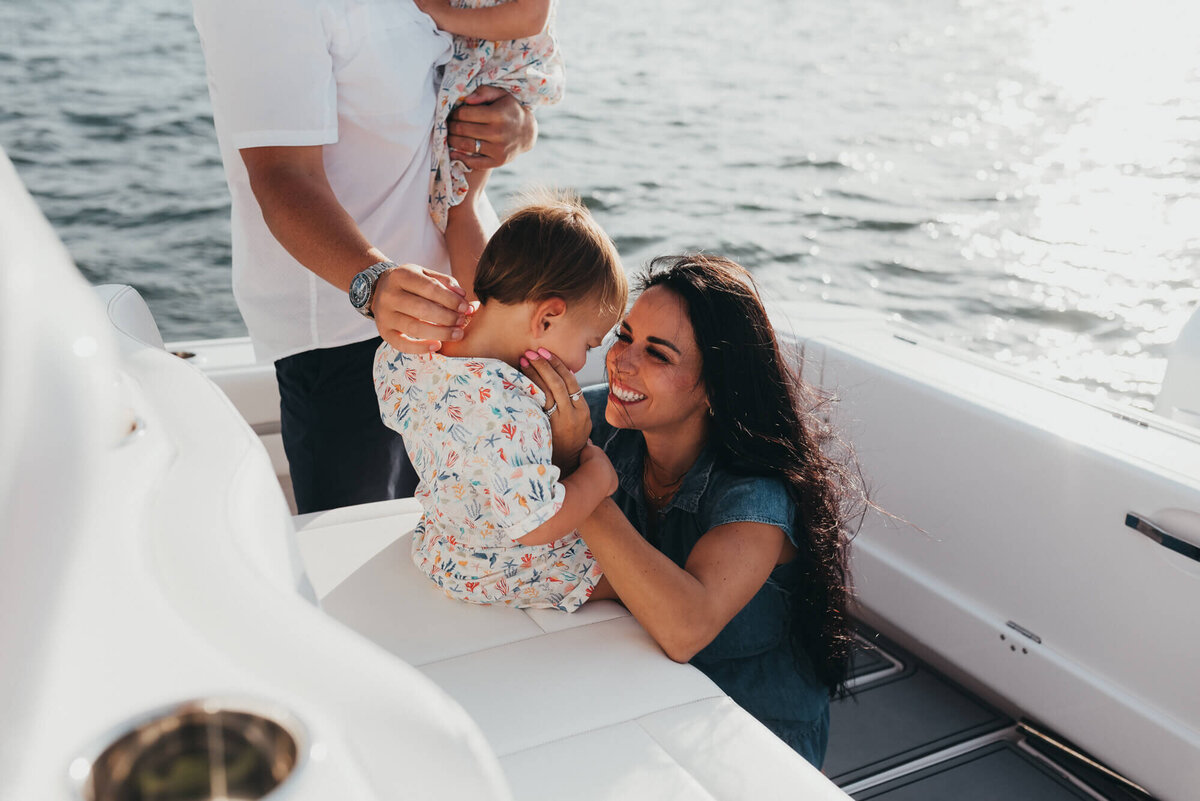 A young mother with long black hair looks lovingly at her son on their family boat during their photoshoot with Allison Wolf, Boston Family Photographer