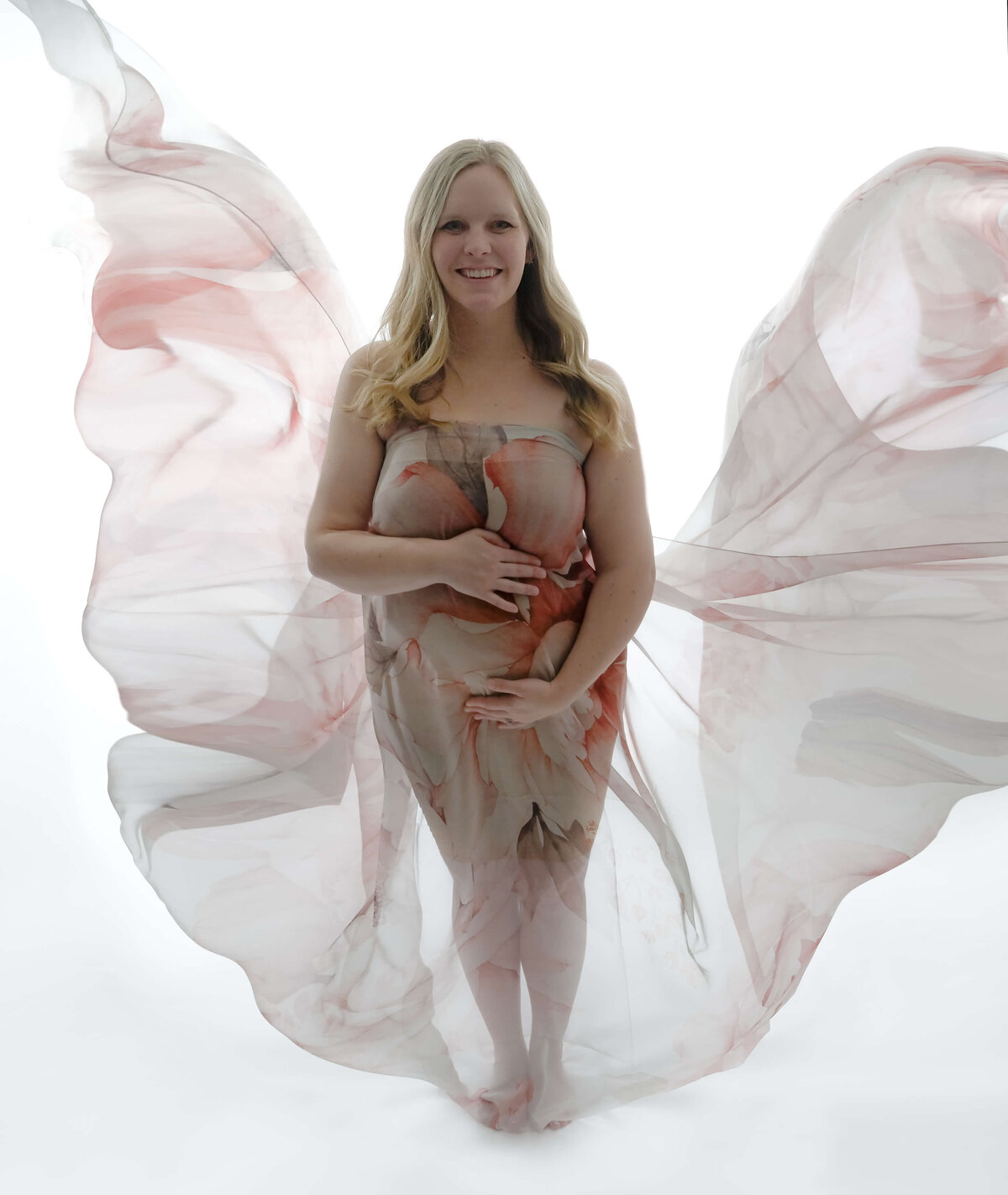 Back lighting during a maternity photo session where subject is wrapped in a sheer floral fabric that is tossed for flowing visual effects.Image by E. Benecki Photography