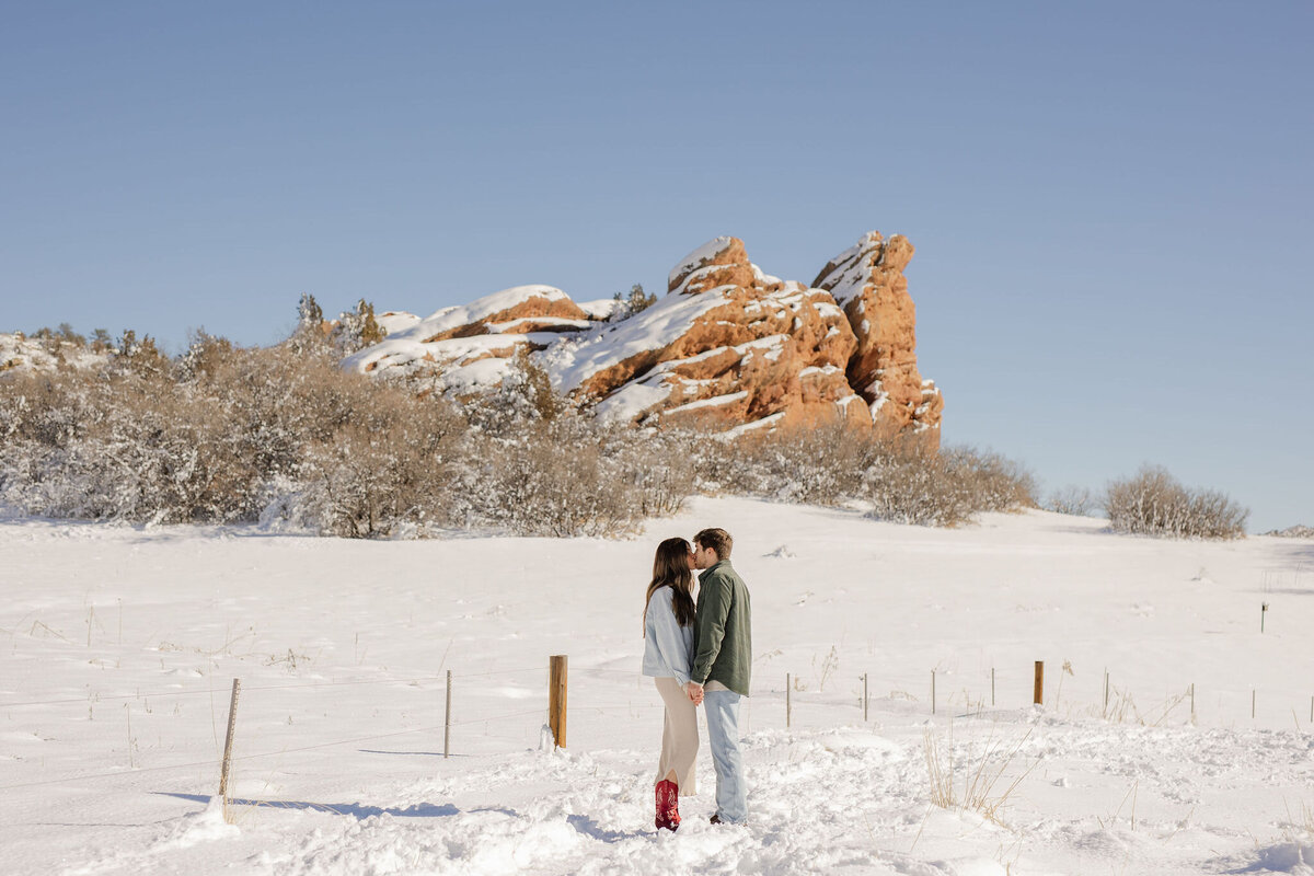 couple kissing in snow with red tock formation in the background