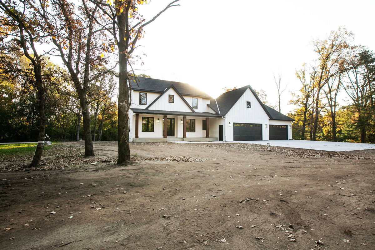 Exterior view of custom home in Big Lake Township, Minnesota with farmhouse details, cream siding, wood pillars and front porch built by Cornerstone Custom Builds