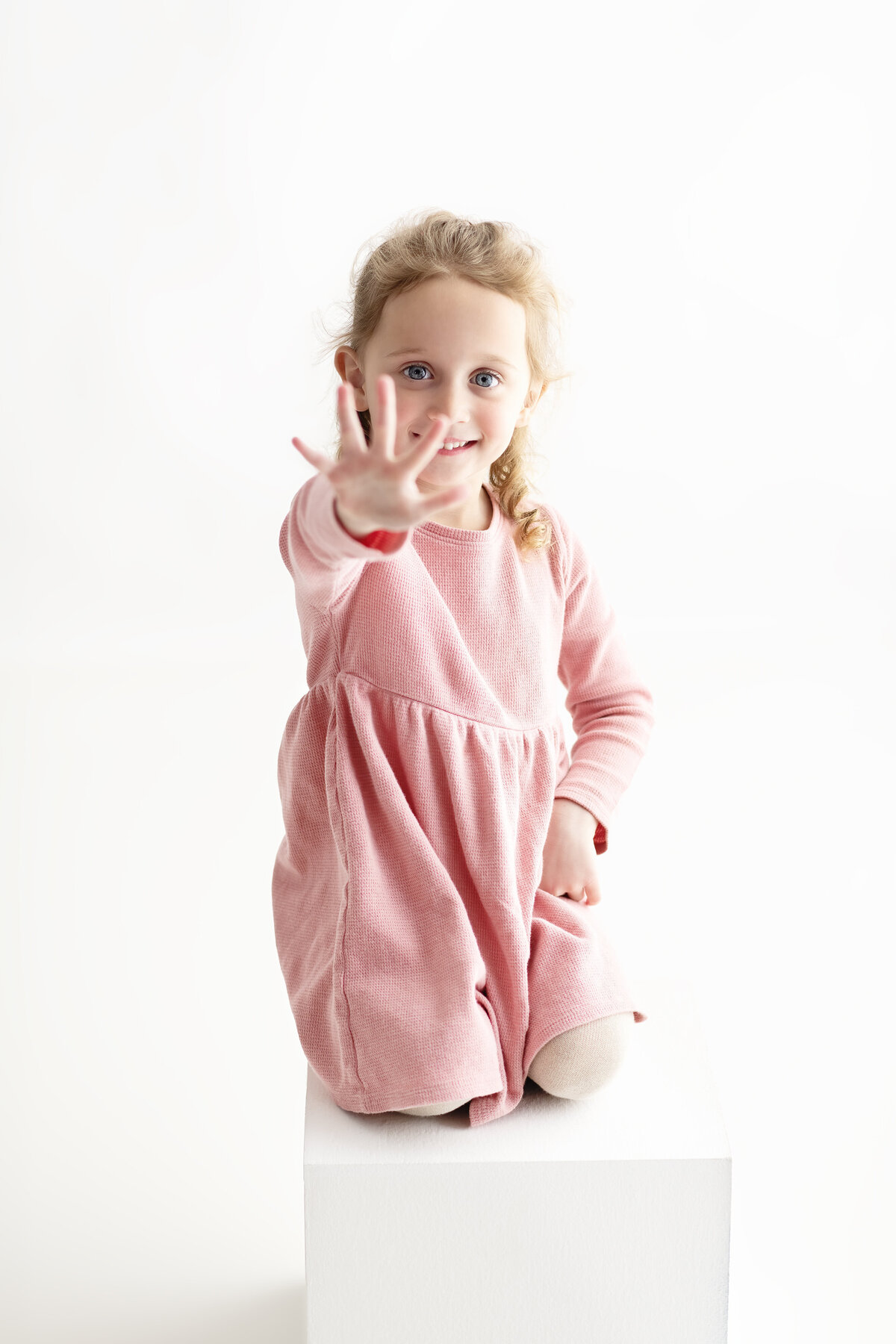 Studio milestone portrait of a smiling girl showing five fingers—celebrating her fifth birthday with confidence and charm.