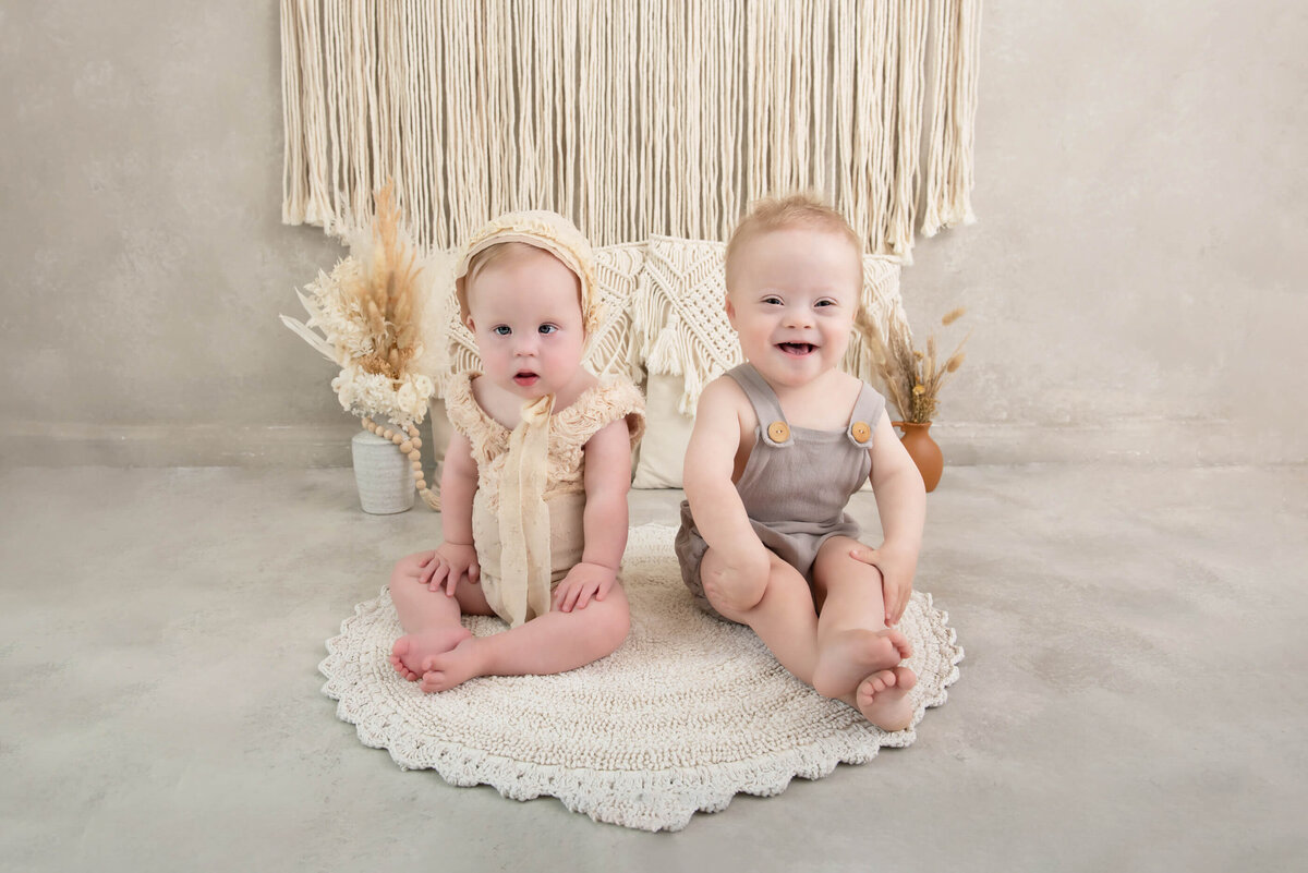 Down syndrome boy and girl wearing beige onesies on a boho style set for their kids family photographer session in Burlington, Ontario 