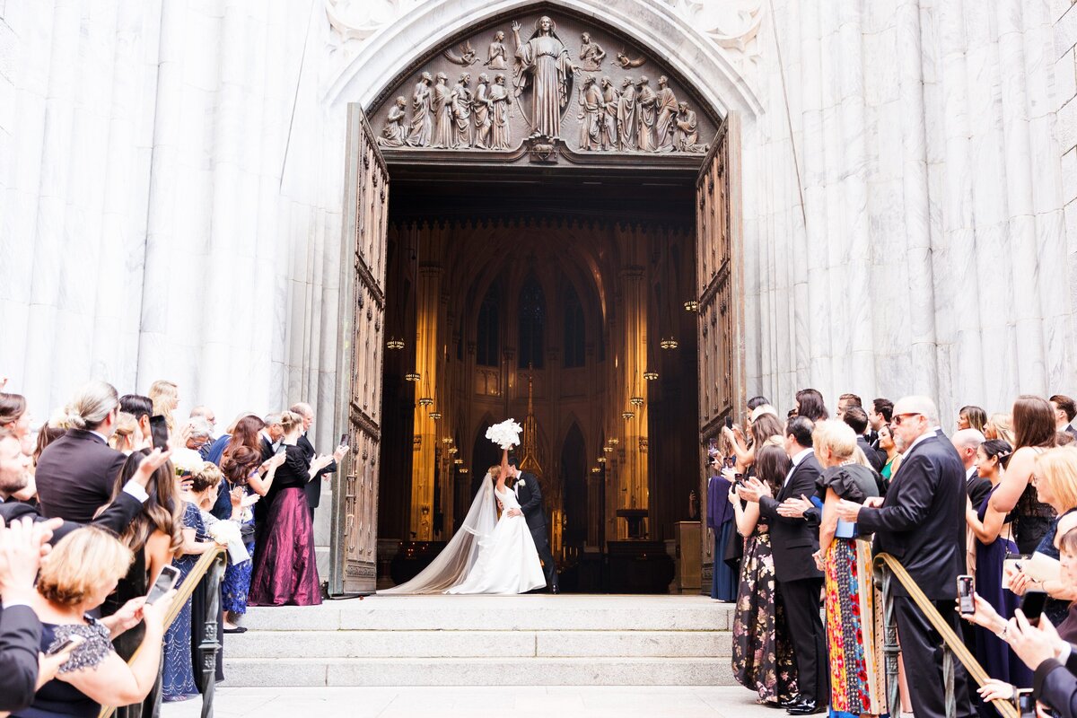 Bride and groom kissing on church steps, celebrated by guests