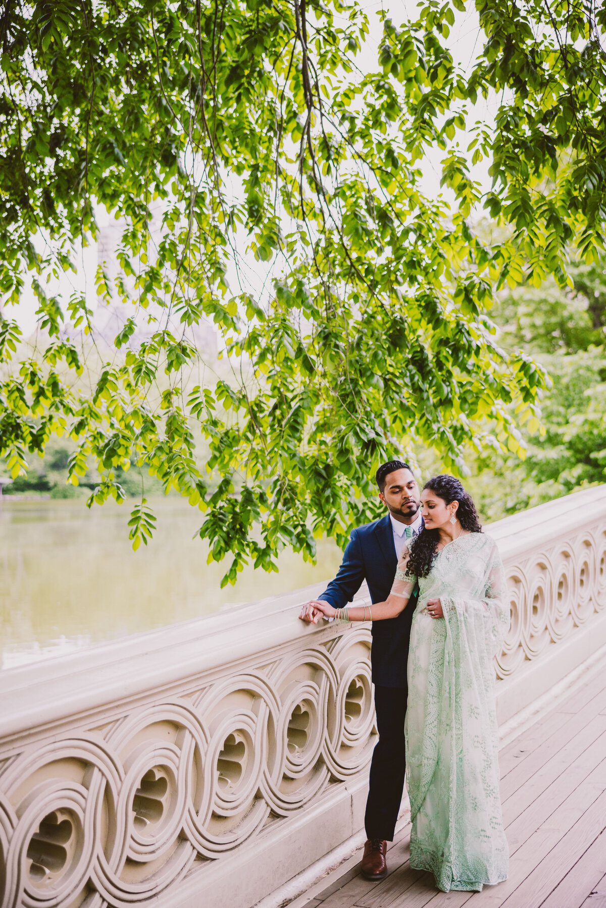 A couple standing in indian outfits on the bow bridge in central park in nyc