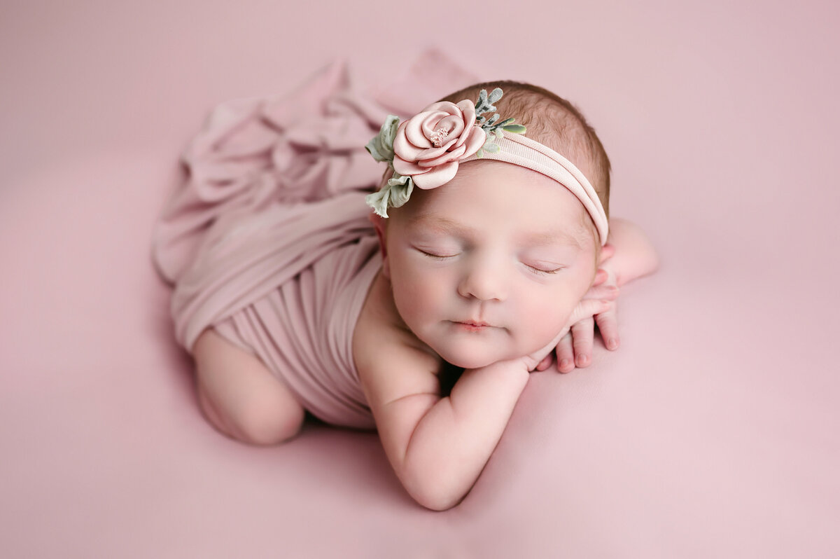 Newborn baby girl lays on her belly with her chin resting sweetly on her hands as she dreams on a pink blanket during her session with the best newborn photographer in Pittsburgh, Katie Louise Photography.