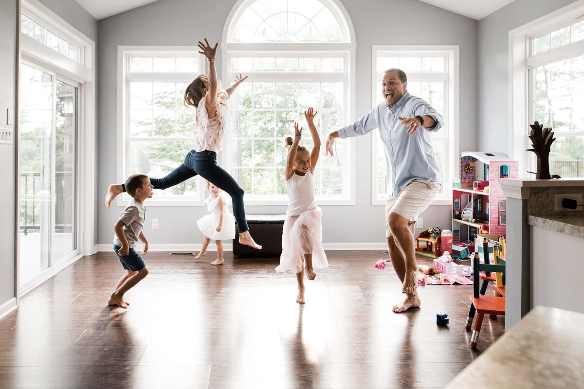 A Pittsburgh family photographer captures a family joyfully jumping together in a bright, spacious living room.