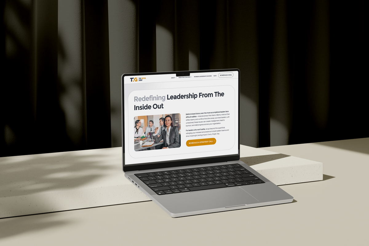 Laptop mockup displaying an executive coach's website design on a cream table against a black wall.