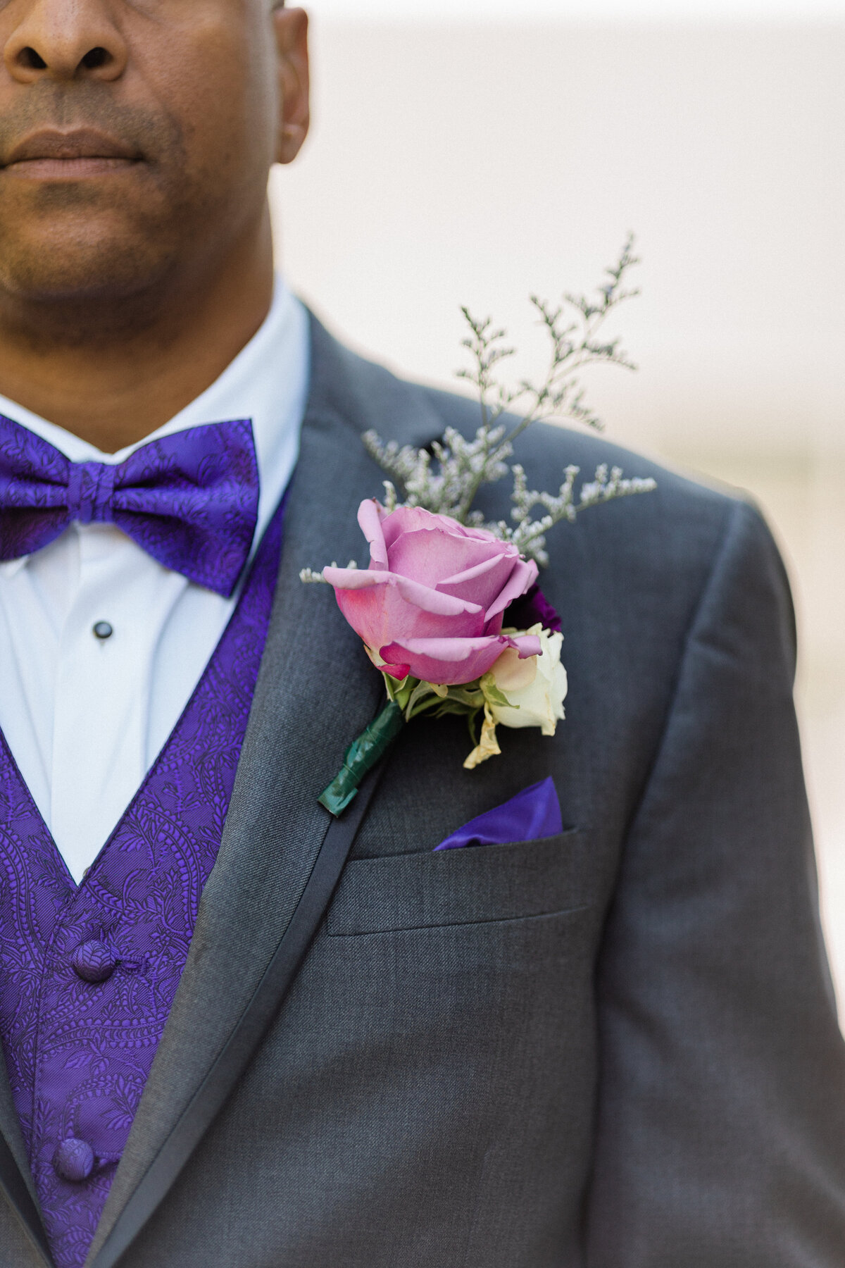 groom wearing a grey suit with a purple vest and purple rose boutonniere