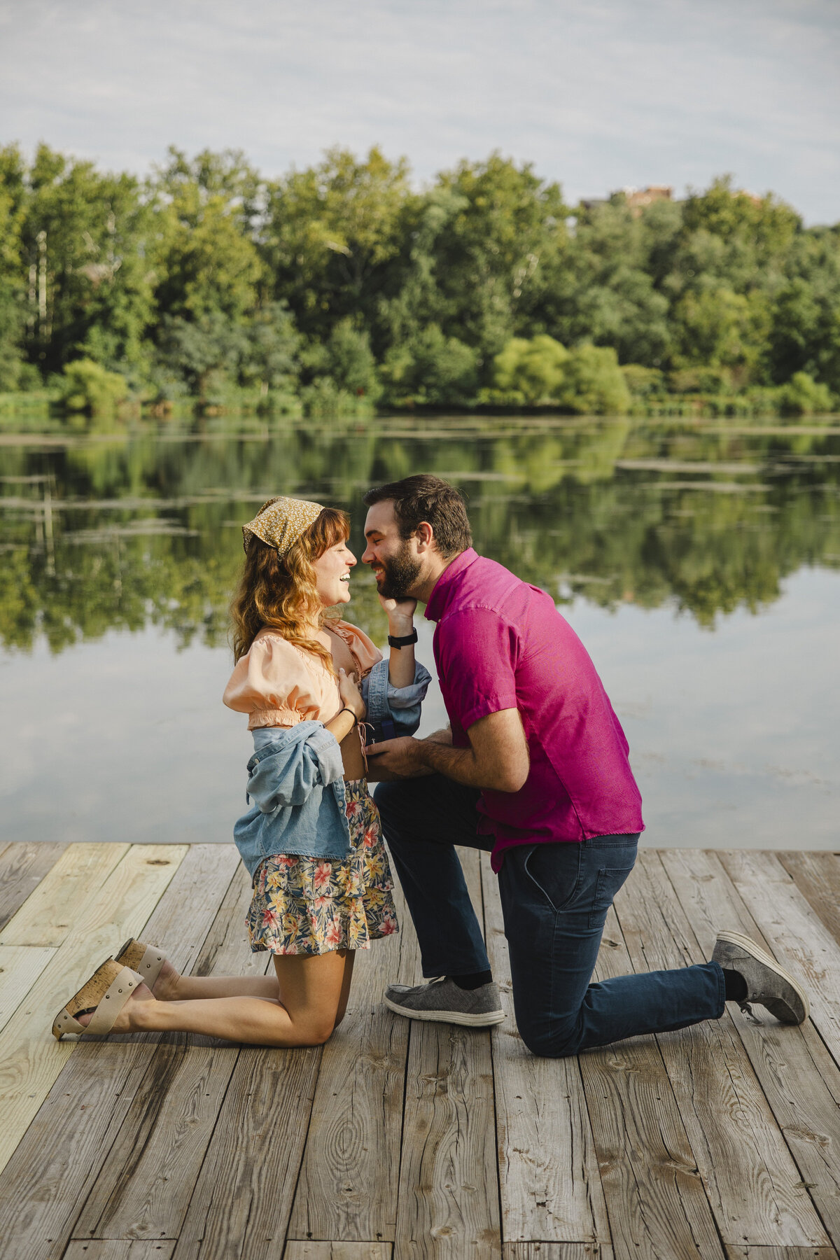 A couple leans in for a kiss in front of a lake.