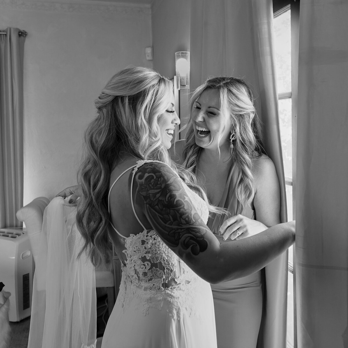 Bridesmaid and bride laugh with each other while getting ready for wedding