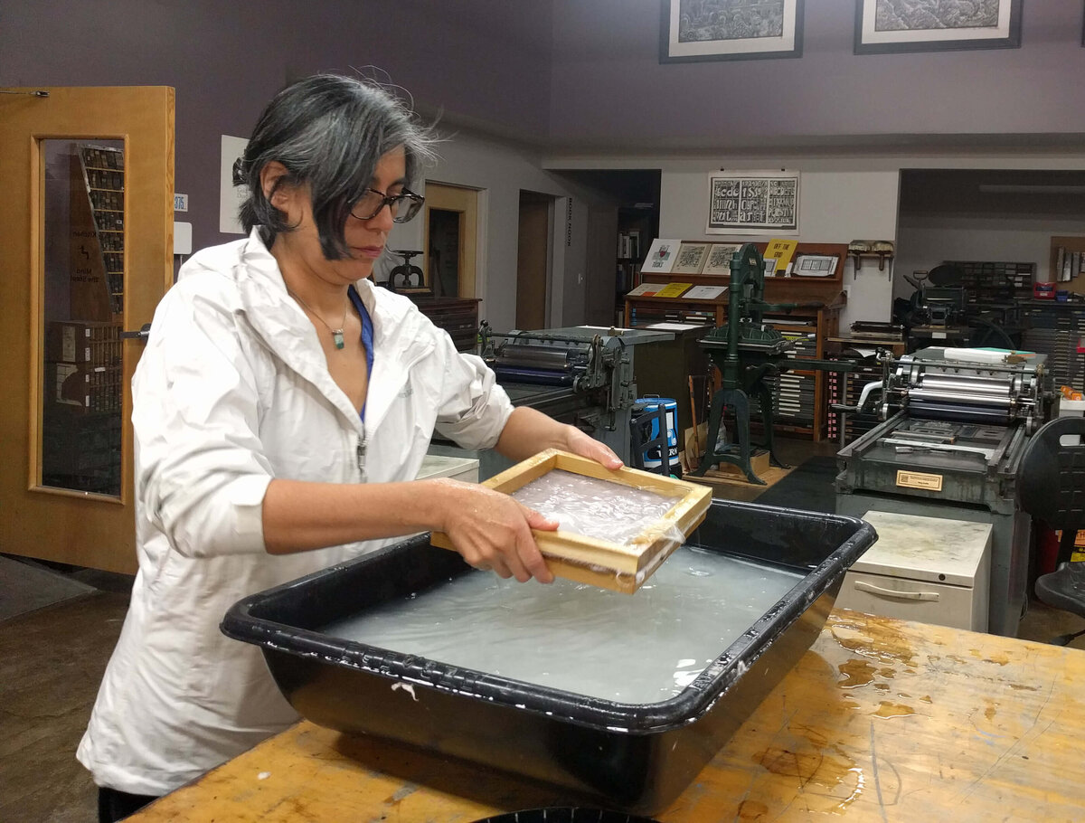 Instructor Michelle Wilson demonstrating the nagashizuki papermaking method with a sugeta at a water vat.