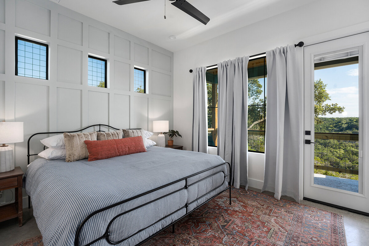 main bedroom with white feature wall, and large windows with view to back porch