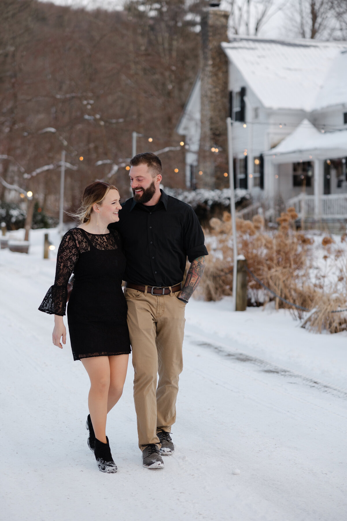 A bride wearing a non-traditional black wedding dress stands against the pristine white snow at The Tillerman Inn in Bristol, Vermont, during her intimate winter elopement ceremony


