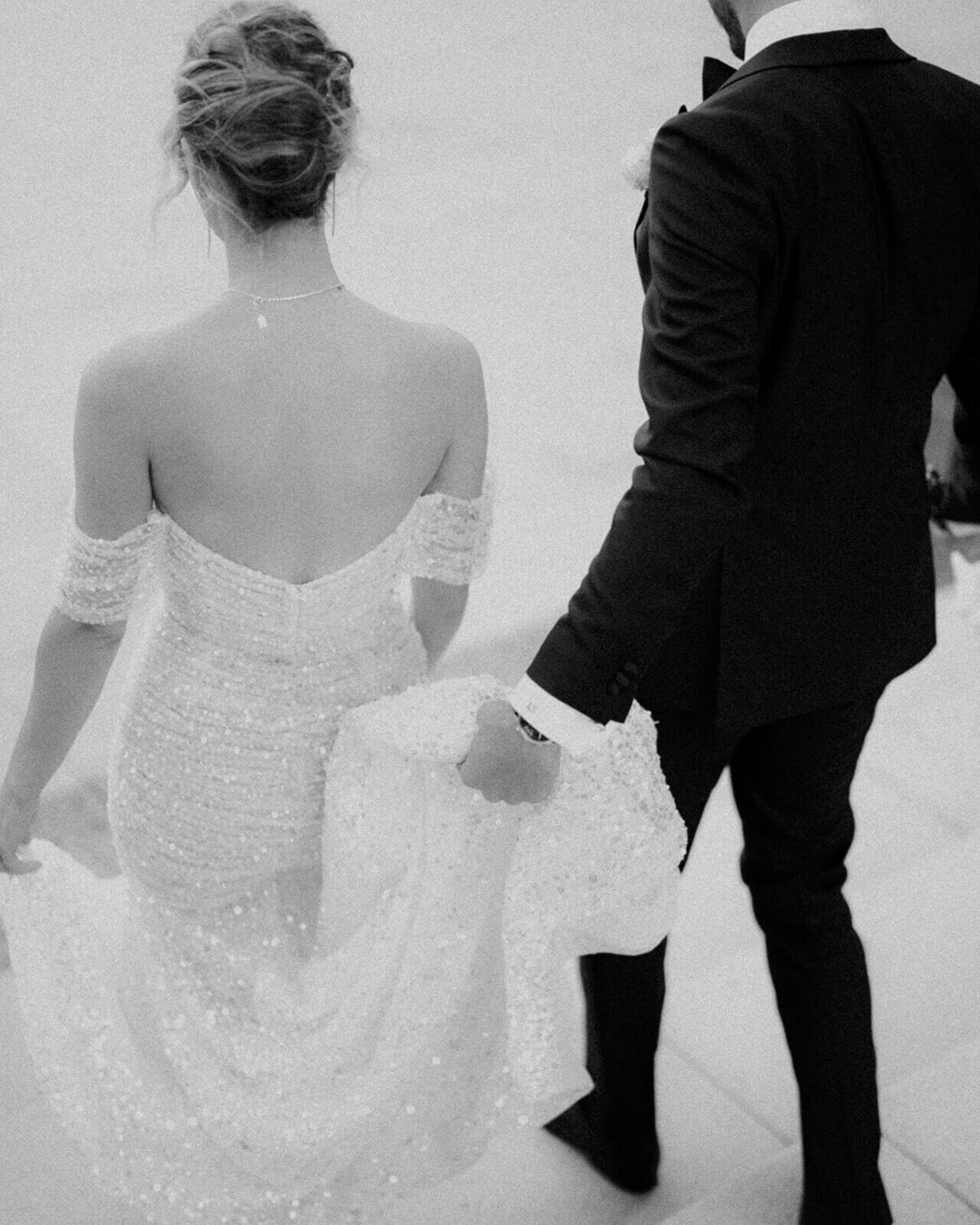 Groom holding the back of the brides dress while walking