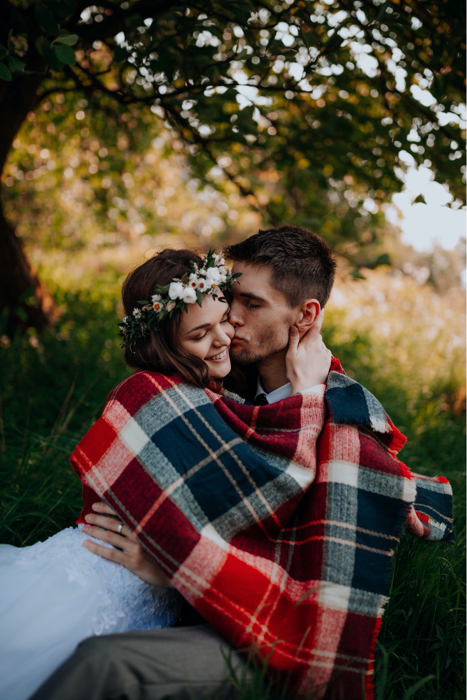 A Bride and Groom hugging in woodland with a tartan blanket  over them