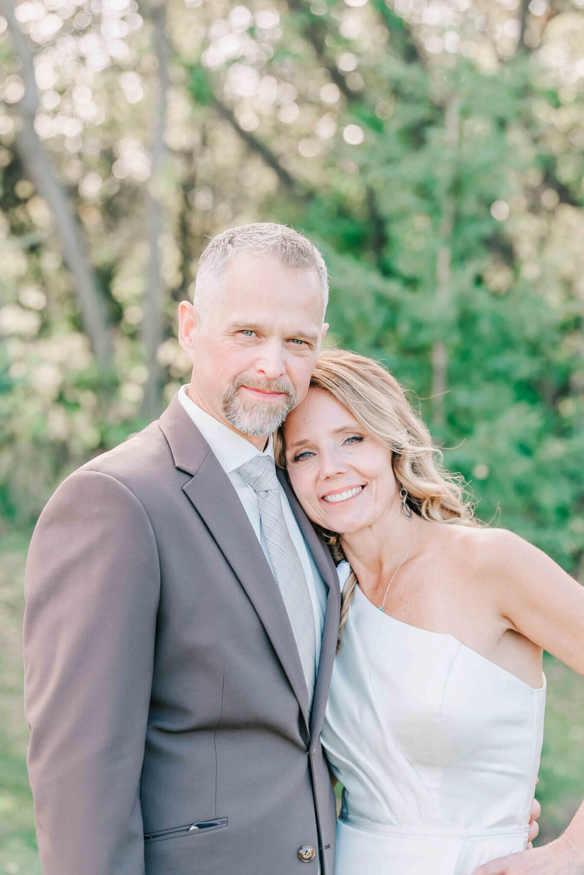 Bride and groom leaning toward each other and looking at the camera. Waist up portrait.