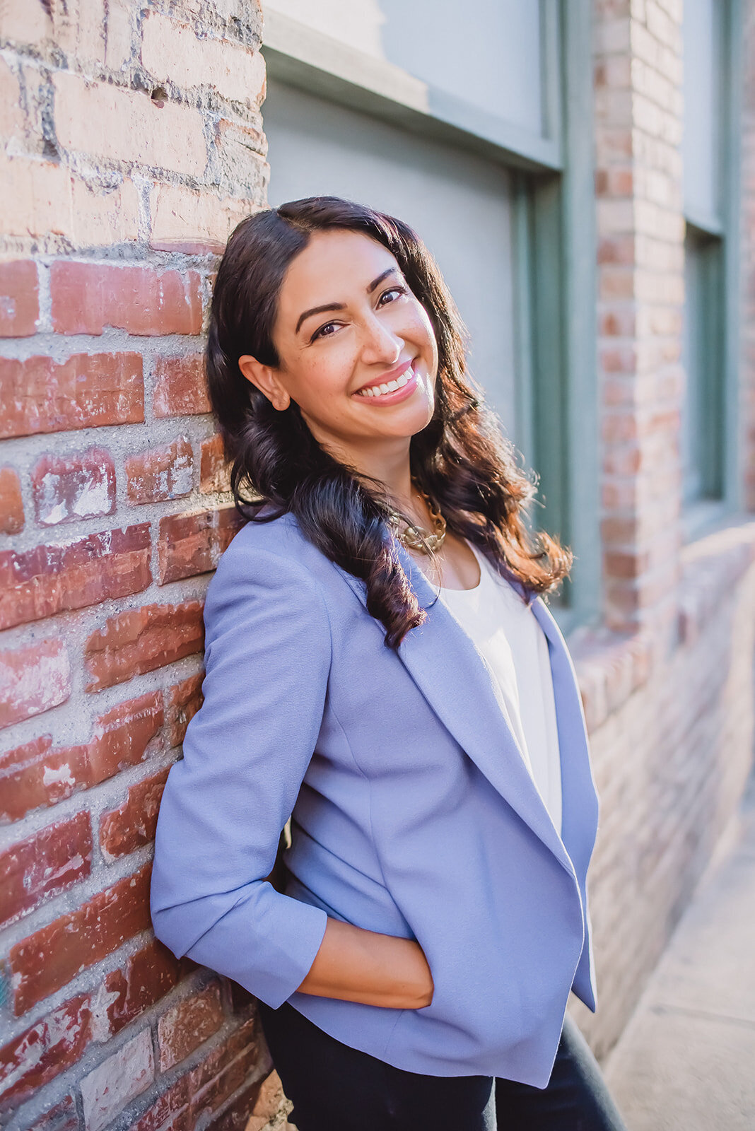 Hajar leans against a brickwall in Los Angeles and smiles for headshots.