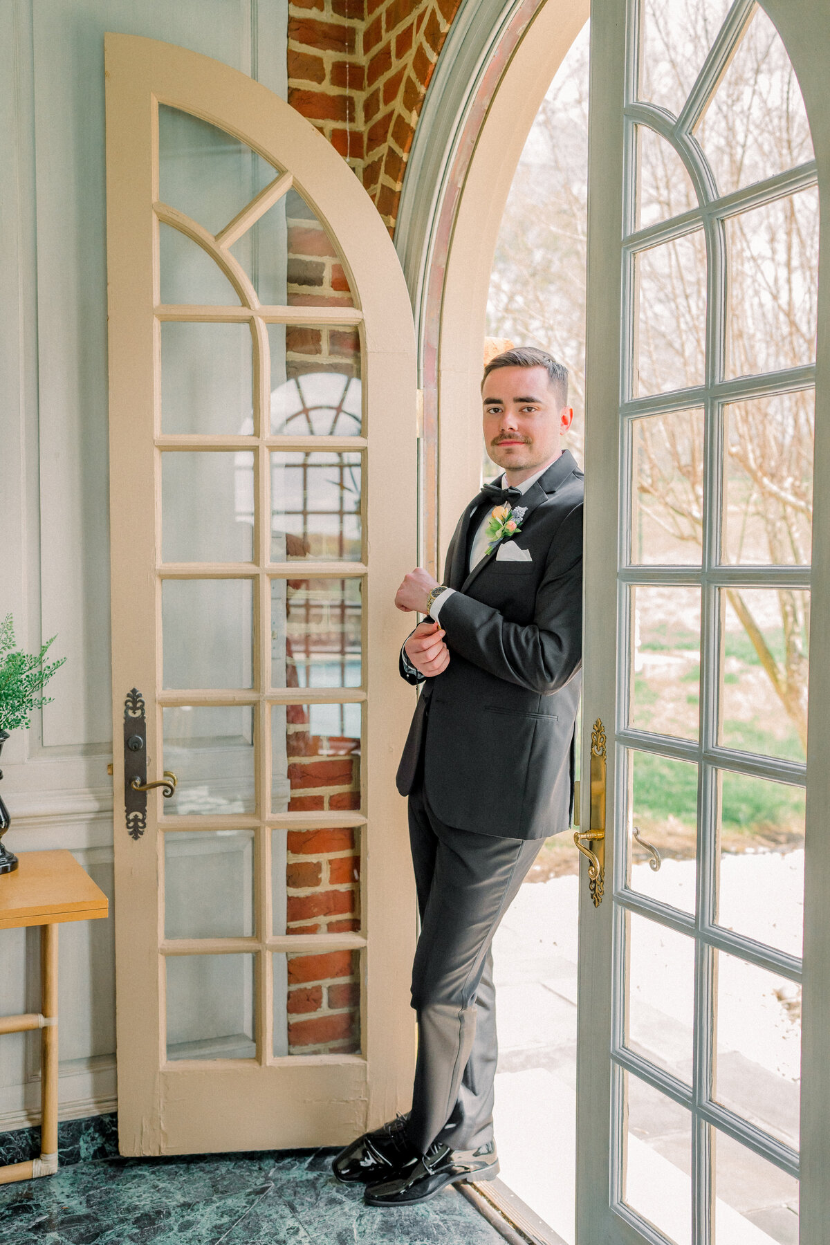 Groom standing in the doorway to the groom getting ready suite adjusting his cufflinks