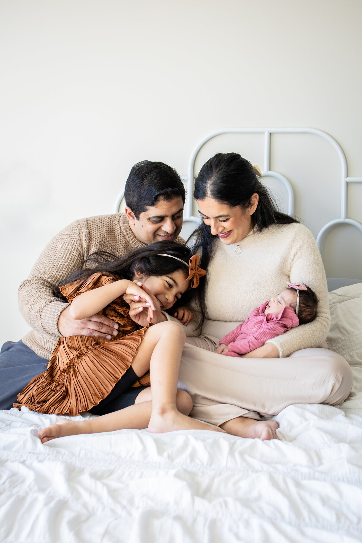 Mom, Dad, Big Sister and Little Sister cuddled on white bed in Boston