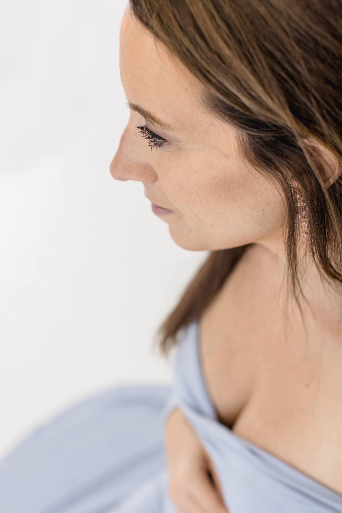 A woman with long brown hair is seen from an elevated angle. She is wearing a light blue off-the-shoulder dress and her eyes are slightly closed. The background is bright, giving the image a soft, serene feel.