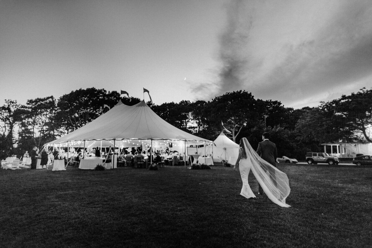 Black and white photo of the bride and the groom walking towards Cape Cod Summer Tent, MA.