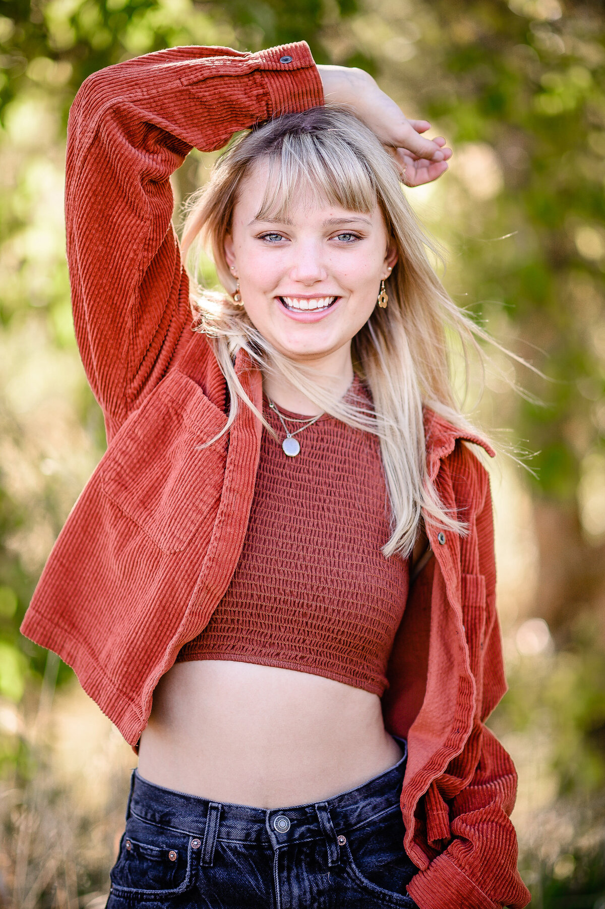 denver senior photographer captures high school senior photo outfit with a burnt orange top and jeans on posing in the woods