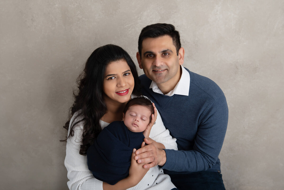 Mom and dad holding newborn baby wrapped in blue for his newborn photos in Burlington, ON