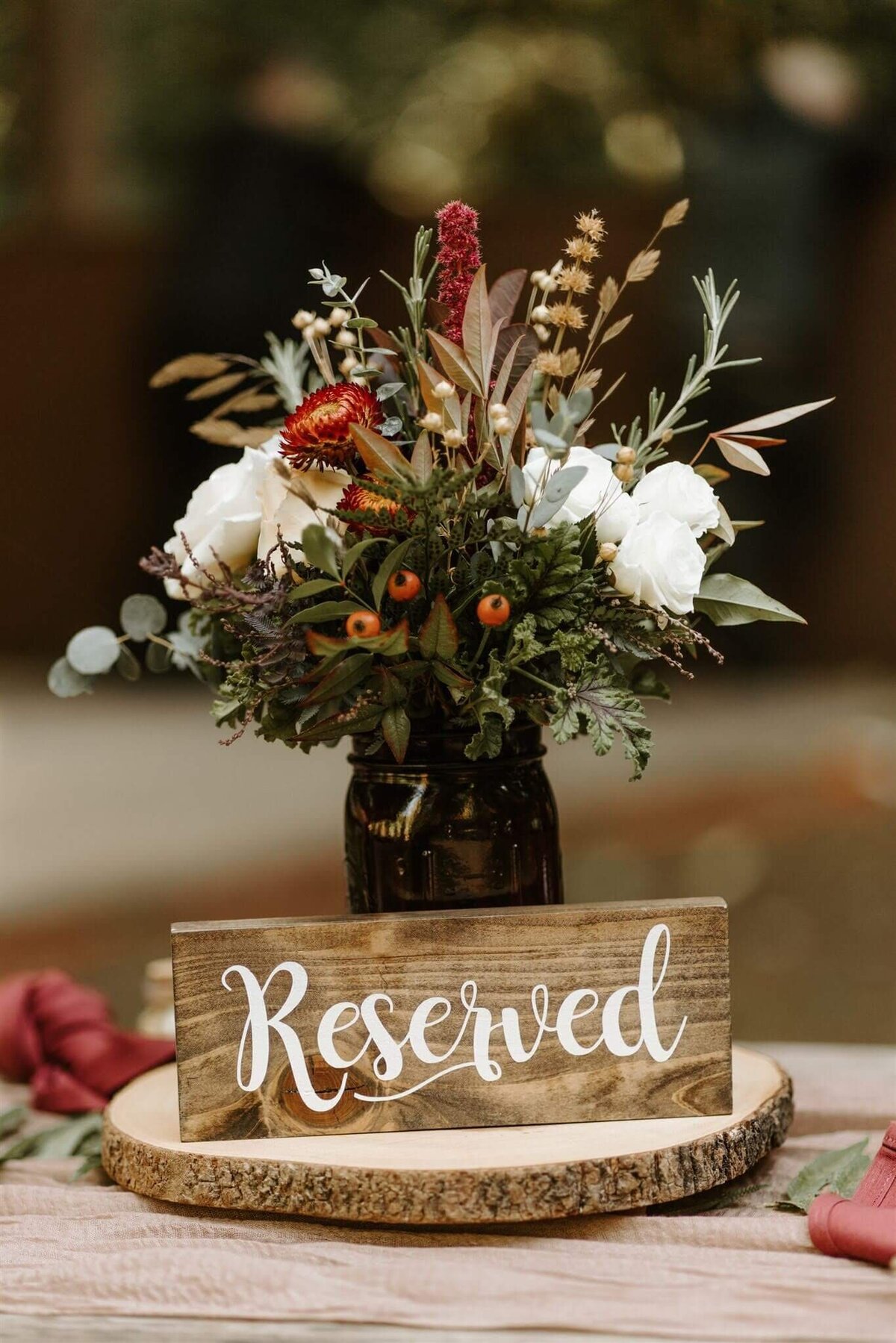 A reserved sign for a table at a wedding reception with a mid-sized floral arrangement behind it.