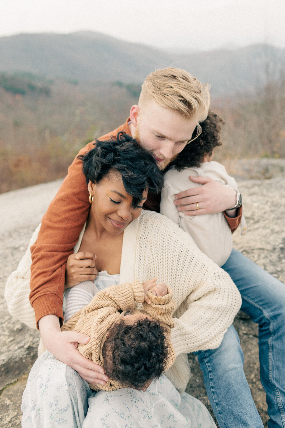 Father leans in to hug mom and both babies in a sweet moment captured during their Kansas City newborn photo session.