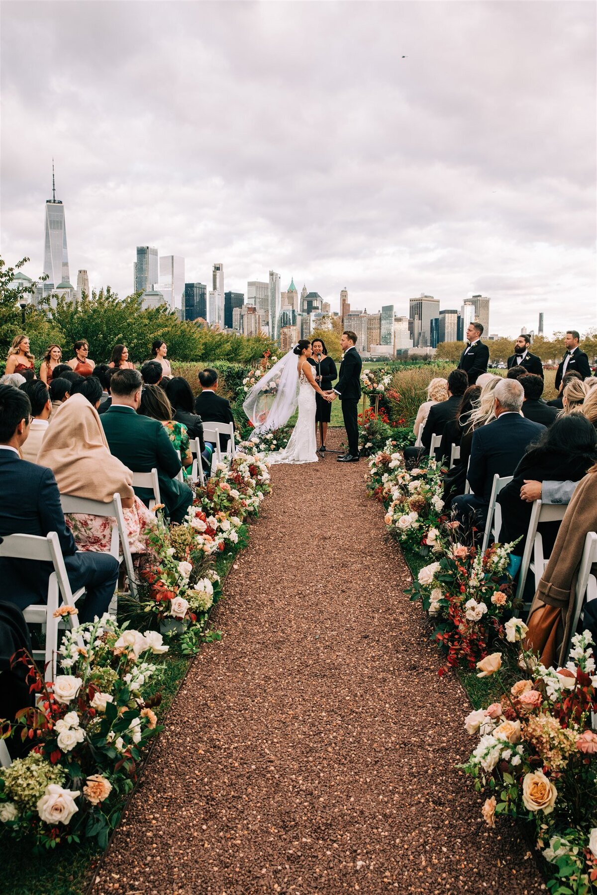 A romantic outdoor wedding aisle lined with lush floral arrangements in warm tones