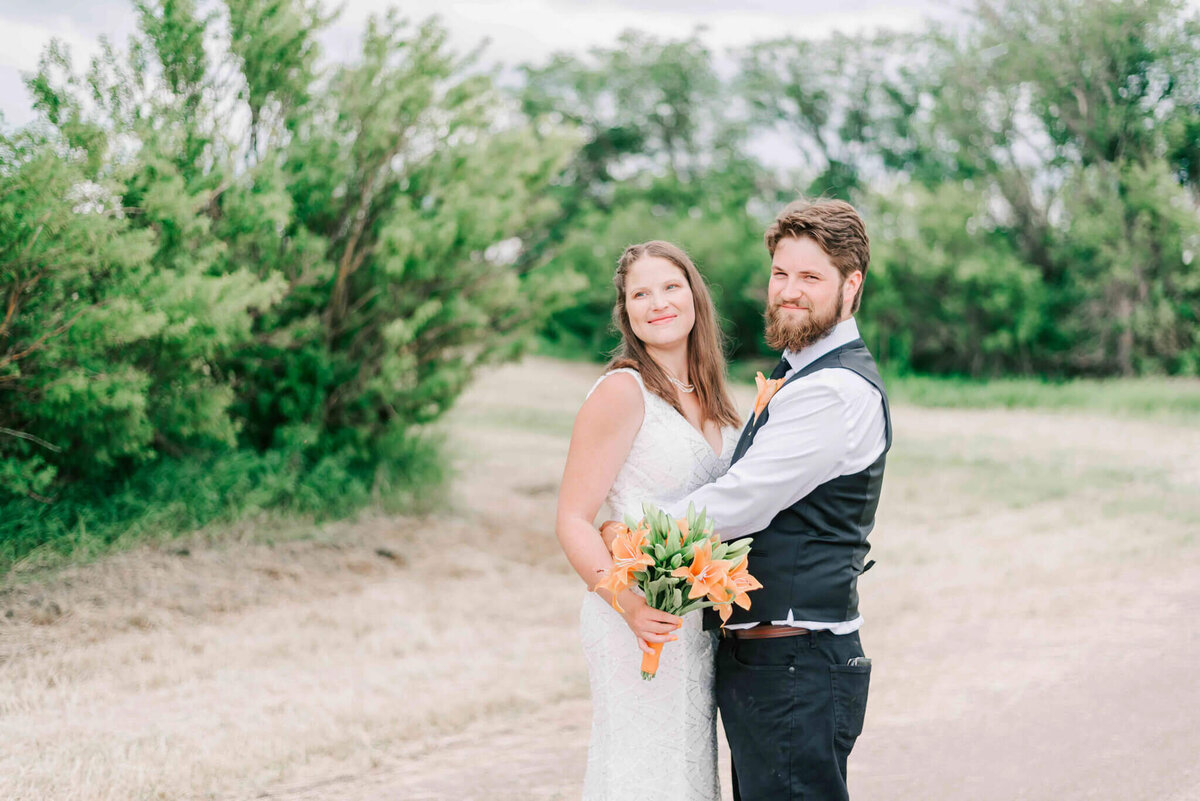 Bride and groom facing each other standing on a gravel road.