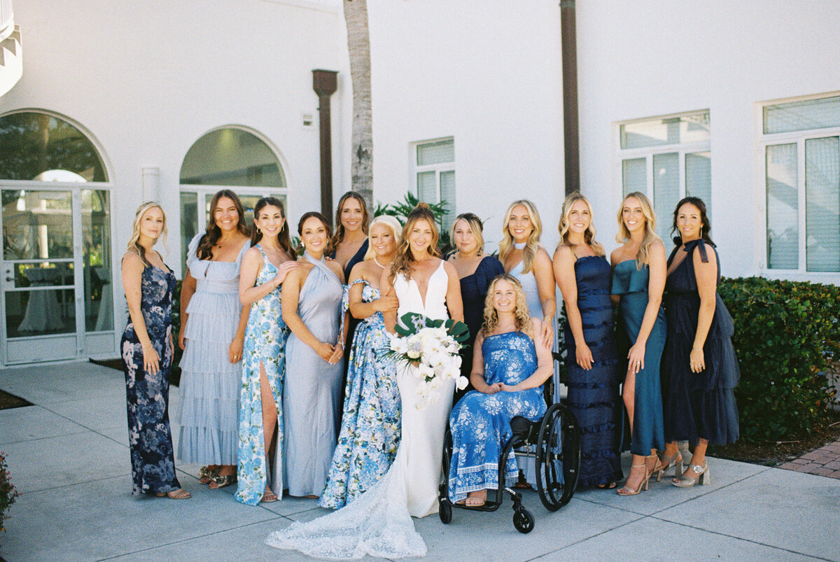 Bride surrounded by bridesmaids in coordinated blue dresses posing together outside wedding venue.