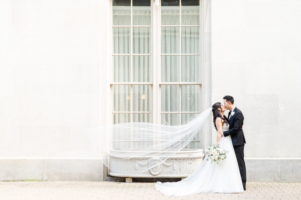 Outside of the Mayflower Hotel in Washington DC bride and Groom kiss with the veil floating in front of large window