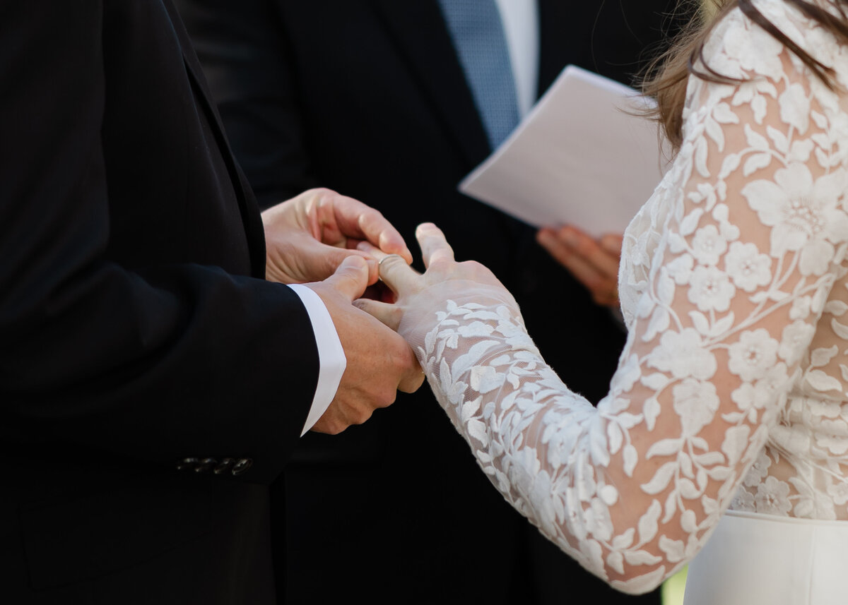 A couple exchanges wedding rings in front of a grand mansion in Stowe, Vermont during their elegant elopement ceremony