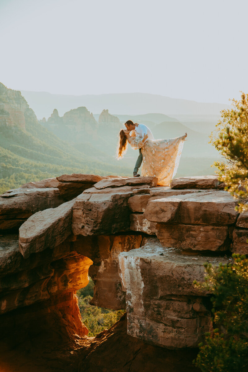 man bows a woman down over a cliff endge in sedona