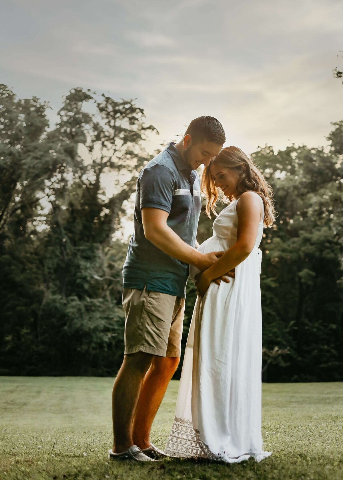 A pregnant couple, photographed by a Pittsburgh maternity photographer, standing in a field at sunset.
