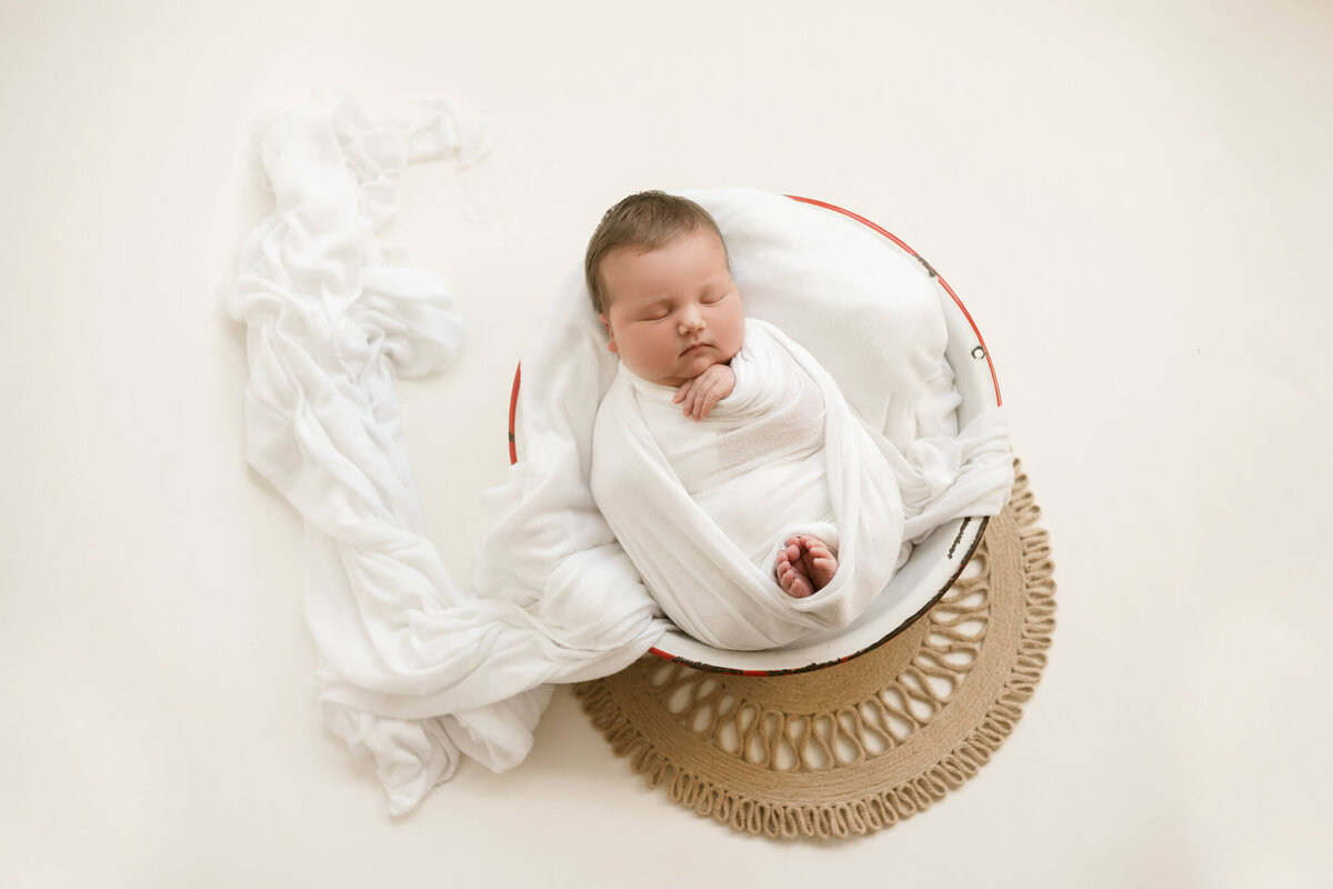 Posed newborn baby  in a white wash bin  wrapped in a white swaddle