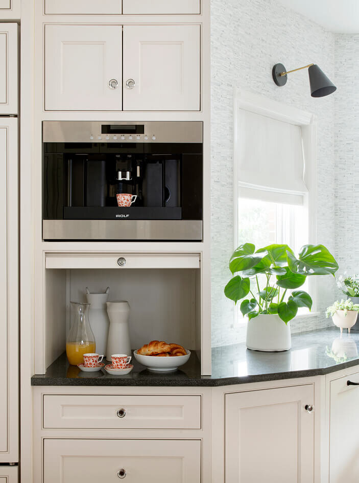 Custom coffee station with Wolf espresso machine and pantry in a white kitchen design with grey counters and oil-rubbed bronze hardware.