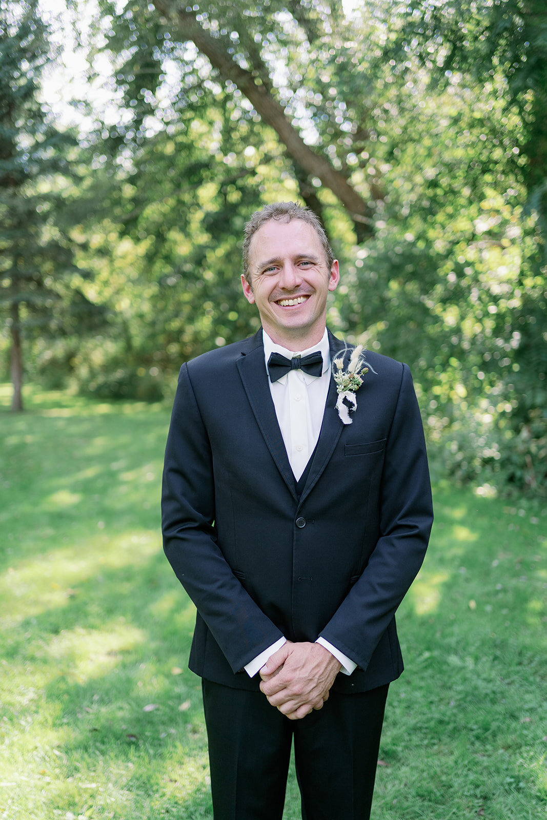 Groom standing in shaded greenery at Glasshouse Community before the ceremony during his summer Michigan wedding.