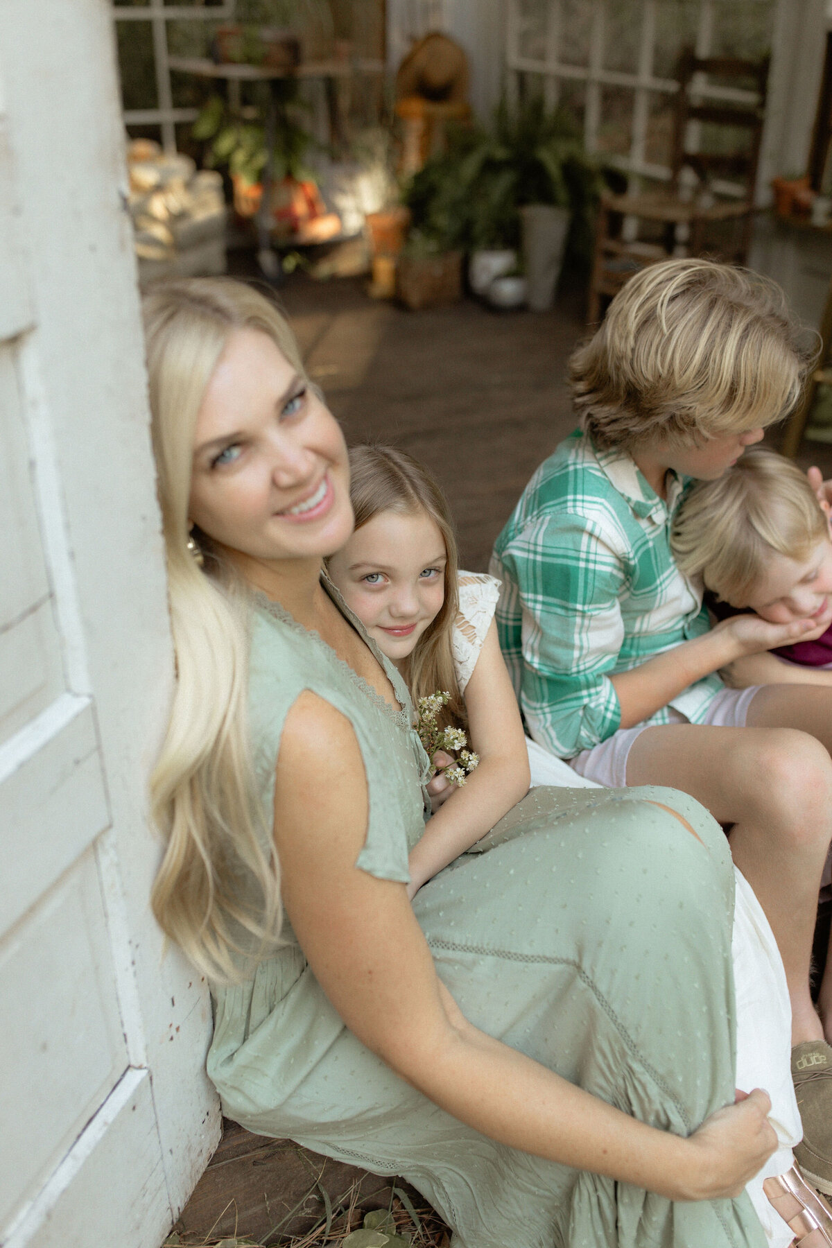 A mother leaning on the door frame of Das Hinterhaus while hugging her daughter as her two other children play. 