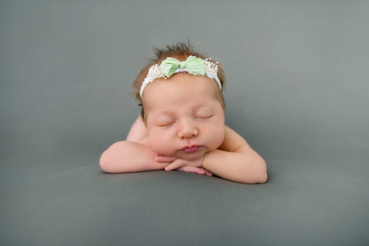 red-haired newborn girl with her head on her hands on a green background for her newborn photography session in Burlington Ontario