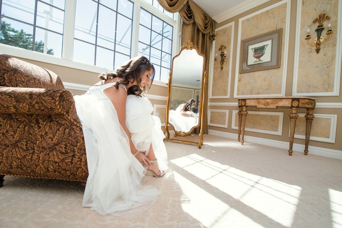 Bride sitting in front of mirror putting on shoes at Stonebridge Country Club