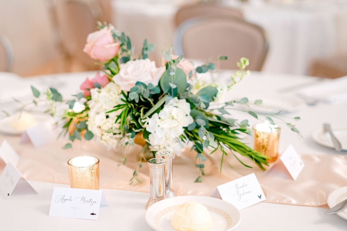 Beautifully arranged wedding table centerpiece with pink and white flowers, surrounded by elegant place cards and candlelit votives.